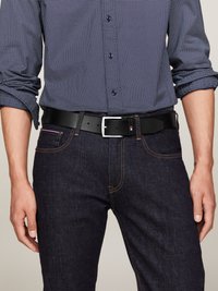 Homme portant une chemise à motifs bleu marine avec les manches retroussées, un jean en denim foncé et une ceinture en cuir noir avec une boucle en argent.