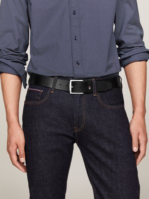 Uomo in camicia patterned blu navy con le maniche arrotolate, jeans in denim scuro e cintura in pelle nera con fibbia argentata.