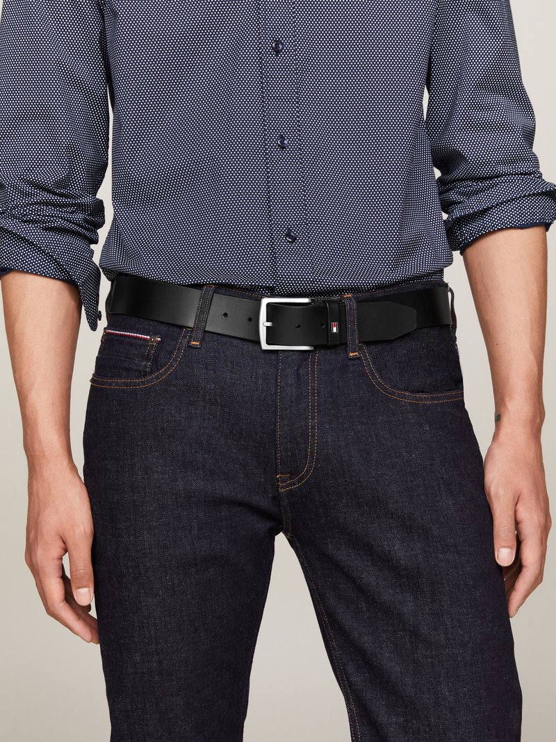 Homme portant une chemise à motifs bleu marine avec les manches retroussées, un jean en denim foncé et une ceinture en cuir noir avec une boucle en argent.