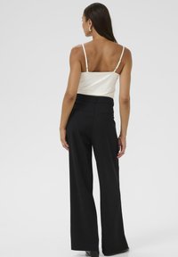 Camisón de satén blanco con tirantes finos, combinado con pantalones de pierna ancha de talle alto en negro, con detalles traseros minimalistas.