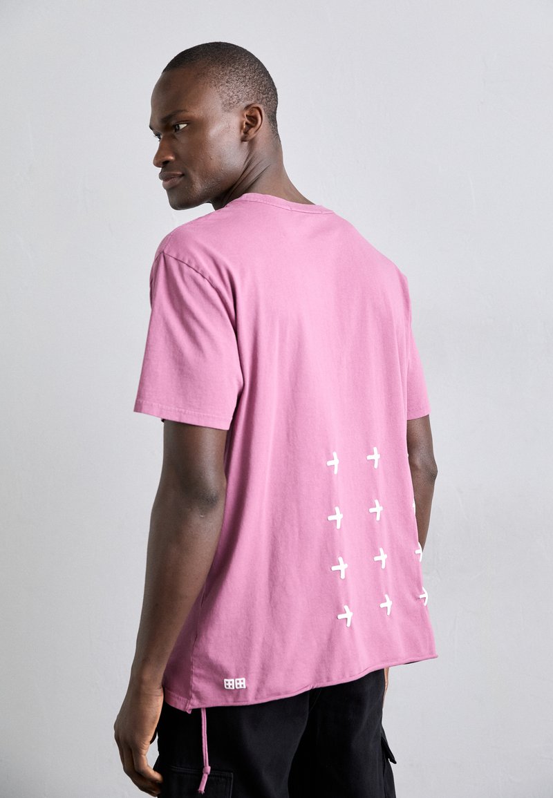 Camiseta de algodón rosa con cuello redondo, mangas cortas y iconos de aviones blancos impresos en la parte posterior. Corte regular con dobladillo cosido.