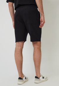 Zwarte katoen shorts met een ontspannen pasvorm, voorzien van een achterzak en een elastische tailleband, gecombineerd met wit en zwarte sneakers.