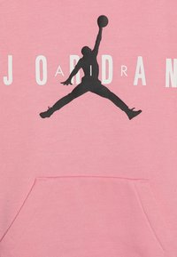 Różowa bluza z kapturem z dużym czarnym logo "Jumpman" na środku. Zawiera białe napisy "JORDAN". Posiada kieszeń z przodu.