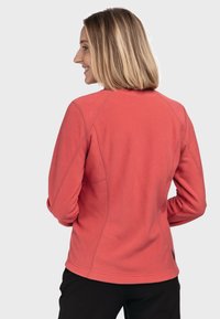 Coralfleecejacke mit strukturiertem Stoff, Raglanärmeln und einem dezenten Nahtdesign. Verfügt über einen schmalen Schnitt und ein Etikett unten links.