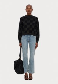 Pull à motif damier noir et or, coupe décontractée ; jean évasé bleu clair ; sac cabas tissé noir ; sandales noires à brides.