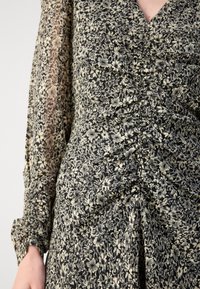 Robe à imprimé floral avec un fond noir, des fleurs crème, des détails froncés et des manches longues bouffantes transparentes. Texture de tissu douce.