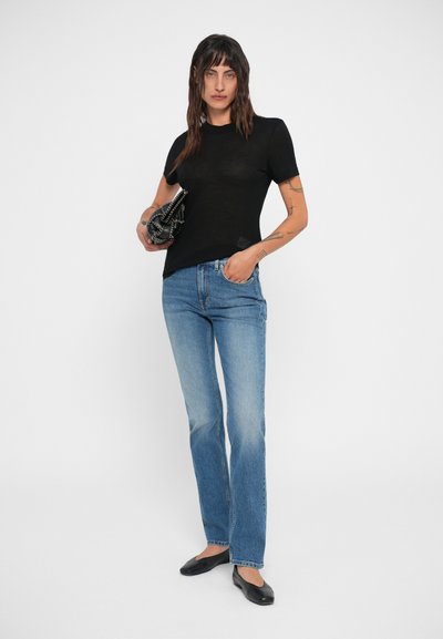 Camiseta negra ajustada de manga corta, combinada con jeans rectos de color azul claro. El modelo sostiene un bolso negro con detalles en texto.