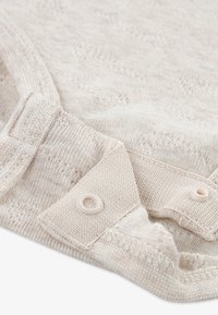 Šviesiai bežinė megzta medžiaga su raštuotu tekstūru, su apvaliu apykakle ir mygtukų uždarymu. Minkšta, lengva medžiaga su subtiliu dizainu.