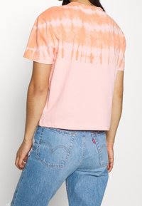 Camiseta de manga corta con un patrón de teñido anudado en degradado de naranja a rosa. Hecha de algodón, con un corte relajado y un cuello redondo.