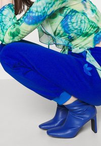 Blue joggers with a logo detail, paired with blue stilettos. The blouse features a sheer, green-to-blue tie-dye pattern.