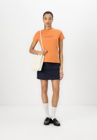 Orange cotton T-shirt with “BOSS” logo, paired with a navy denim skirt, white knee-high socks, and black loafers, plus a cream tote bag.