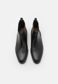 Botas de cuero negro hasta el tobillo con punta afilada, textura suave, paneles laterales elásticos y una pequeña lengüeta en la parte trasera para facilitar su uso.