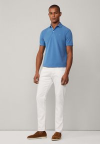 Blaues kurzärmliges Poloshirt aus Baumwolle, kombiniert mit weißen Hosen und braunen Wildleder-Schlupfschuhen. Schlichtes Design mit einem Kragen.