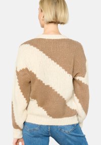 Pleteni pulover s kremasto in bež geometrijskim vzorcem, teksturirano tkanino, udobnim krojem ter rebrastimi manšetami in robom.