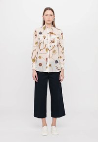 Camicia a maniche lunghe, trasparente, con motivi floreali e astratti multicolori. Presenta due tasche frontali e una patta con bottoni, abbinata a pantaloni neri a gamba larga.