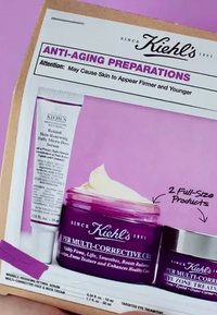 Lilla krukke og sølv-låg beholder med Kiehl's anti-age produkter med hvid creme. Tekst med produktdetaljer på en lyserød baggrund.