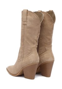 Bézs színű műbőr cowboy csizma, ferde szárú, hegyes orrú, rétegezett sarokkal. Díszítve varrási részletekkel és felhúzófülekkel a könnyű viselet érdekében.