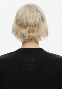 Black t-shirt with short sleeves, featuring a textured, tonal printed design on the back with script style text. Soft fabric.