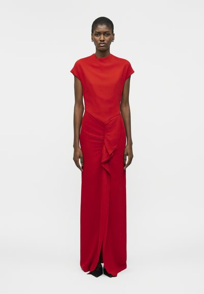 Tall woman with short hair wearing a floor-length red dress with a high neckline and ruched detail down the front center.
