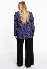 Blazer à motifs noir et violet avec des manches longues, présentant des lignes ondulées. Assorti à un pantalon large noir. Texture de tissu lisse.