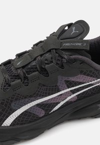 Chaussure de course noire avec une tige en mesh, accents gris, détails réfléchissants et semelle texturée pour une meilleure adhérence et stabilité.