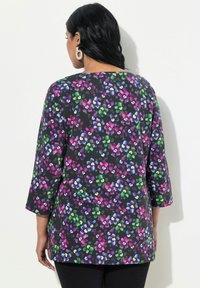 Tunika a stampa floreale con maniche ¾, caratterizzata da uno sfondo nero e fiori vivaci di colore viola, verde, blu e giallo. Tessuto con una superficie liscia.