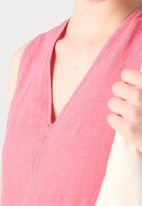 Ärmelloses V-Ausschnitt-Top aus weichem rosa Stoff mit sichtbaren Nähdetails. Glatte Textur und lockere Passform, kombiniert mit einer hellen Tasche.
