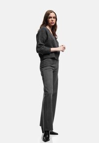 Grijze gebreide cardigan met V-hals en knoopsluiting, gecombineerd met grijs gestreepte rechte broek en zwarte puntige hakken.