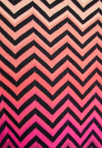 Strikket stof med et zigzag-mønster i sort, pink og koralfarver; har en gradienteffekt fra mørk til lys.