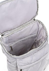 Mochila gris acolchada con apertura superior, que muestra un interior espacioso y un bolsillo con cremallera en la parte trasera. Textura suave y lisa.