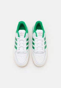 Tenis brancos com três riscas verdes, colarinho acolchoado, biqueiras perfuradas e atacadores brancos. Sola de borracha com um acabamento texturizado.