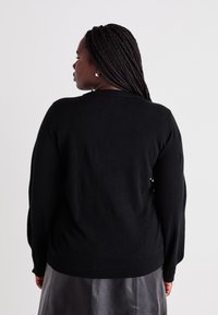 Schwarzer Strickpullover mit rundem Halsausschnitt und langen Ärmeln. Glatte Textur und figurbetontes Design, endet auf Taillenhöhe.