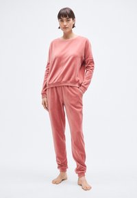 Ensemble de vêtements de détente en velours rose comprenant un haut à manches longues avec col rond et poignets élastiques, accompagné d'un pantalon fuselé avec ceinture élastique.