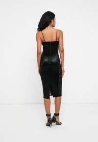 Μαύρο βελούδινο midi φόρεμα με λεπτές τιράντες, εφαρμοστή σιλουέτα, φερμουάρ στην πλάτη και λευκές λεπτομέρειες στα πλάγια. Διαθέτει πίσω σχισμή για άνεση στην κίνηση.