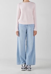 Pull en laine rose clair, coupe décontractée, encolure ronde. Jean bleu clair ample, jambes larges, associé à des baskets noir et blanc.