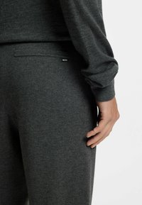 Szary sweter o miękkiej fakturze i luźnym kroju. Posiada małą czarną metkę "BOSS" z boku, z długimi rękawami i zaokrąglonym dekoltem.