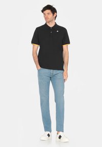 Polo nero con dettagli arancioni alla colletto, indossato con jeans azzurri chiari e sneakers bianche. Presenta un piccolo logo sul petto.