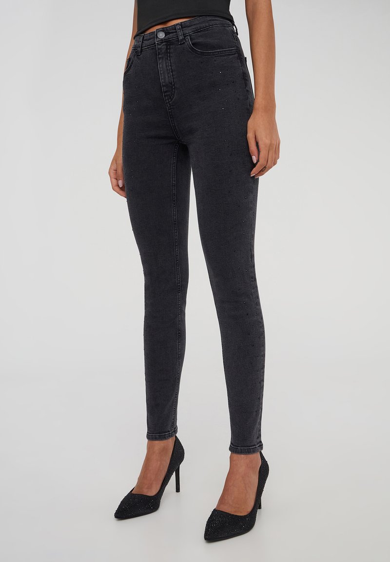 Czarne jeansy skinny z wysokim stanem, z delikatnymi akcentami ćwieków wzdłuż nogawek. Tkanina jest gładka i lekko elastyczna.