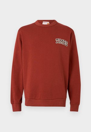 Bordeaux hettegenser laget av mykt stoff, med rund hals, ribbestrikkede mansjetter og brystbroderi med teksten "TIMBS" i hvit skrift.