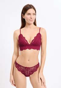 Burgunderroter Spitzen-Bralette mit wellenförmigen Rändern, verstellbaren Trägern und passendem Spitzen-Slip mit einer Schleifendetail in der Mitte und filigranen Mustern.