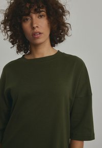 Olive green cotton t-shirt with a round neck, short sleeves, and a relaxed fit, featuring minimal stitching details.
