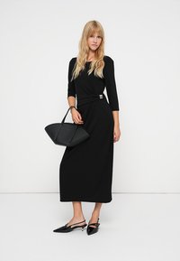 Czarna sukienka z długim rękawem, dopasowana w talii z lekko rozkloszowanym dołem. Posiada metaliczny akcent w talii. W zestawie z czarną, sztywną torebką.