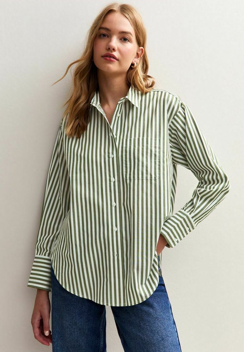 Green and white striped button-up shirt with a classic collar, long sleeves, and a front pocket, paired with casual blue jeans.
