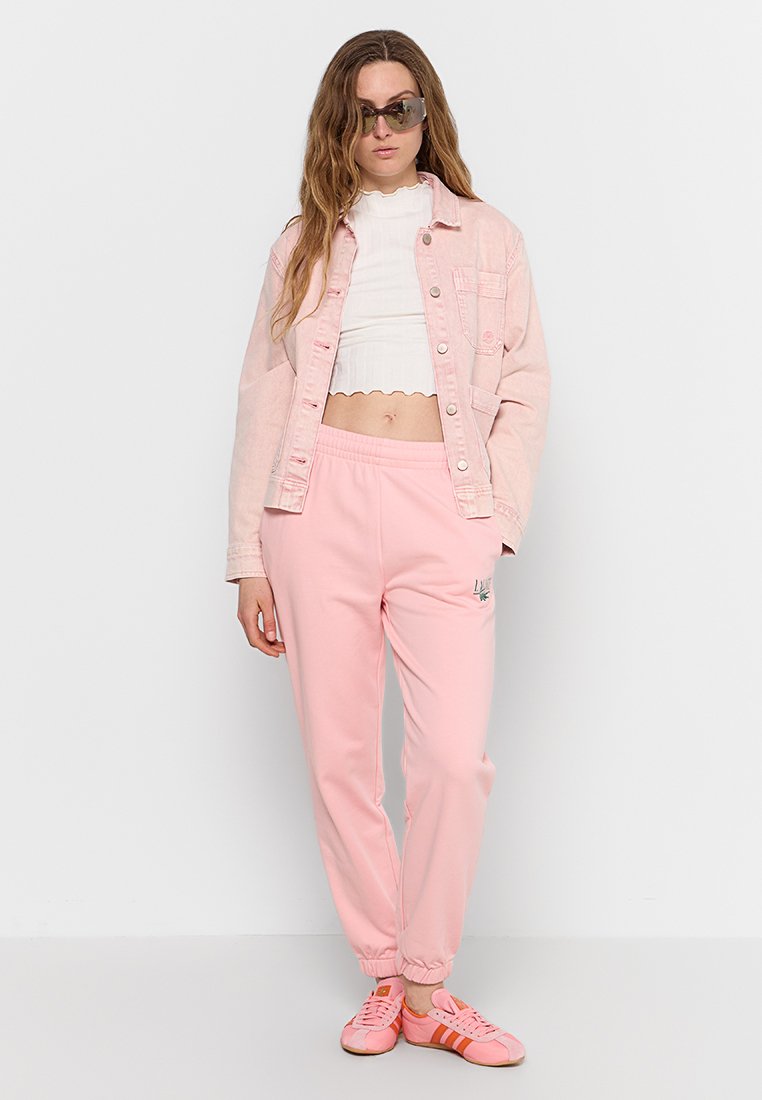 Roze denimjack, witte geribbelde crop top en roze joggers met elastische manchetten. Accessoires zijn onder meer een zonnebril en roze sneakers.
