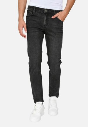Jeans in denim nero con vestibilità slim, dotati di cinque tasche, chiusura frontale con bottone e una texture liscia. Indossati con sneakers bianche.