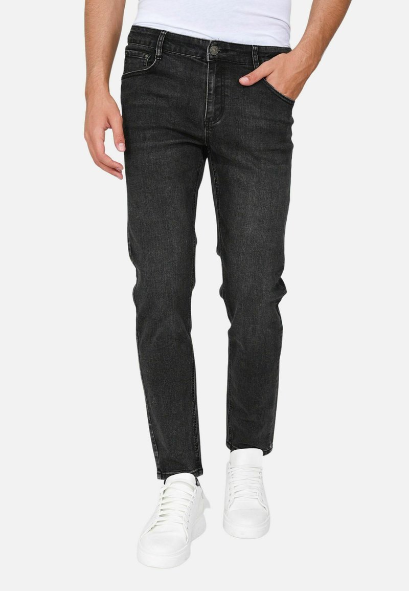 Jeans in denim nero con vestibilità slim, dotati di cinque tasche, chiusura frontale con bottone e una texture liscia. Indossati con sneakers bianche.