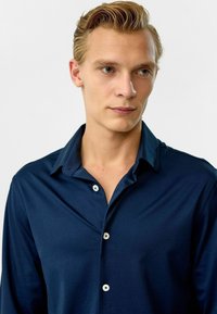 Navyblauwe lange mouwen shirt gemaakt van gladde stof, met een button-down kraag en witte knopen langs de voorste sluiting.