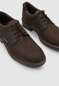 Zapatos de cuero marrón con cordones, con punta redondeada, detalles cosidos y un acabado texturizado. Suela de goma negra para mayor durabilidad.