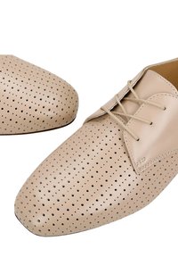 Chaussures en cuir beige à lacets avec un design perforé sur l'avant et les côtés, montrant des détails en gros plan de la texture et des coutures.