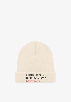 Bonnet en tricot beige avec un revers plié. Présente un texte noir et un graphique de cœur rouge disant : « Un peu de ceci dans ce monde brutal (mais pas trop). »